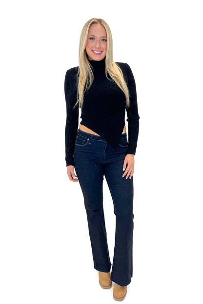Front view of woman wearing Black Ribbed Asymmetrical Top with jeans against white studio background.