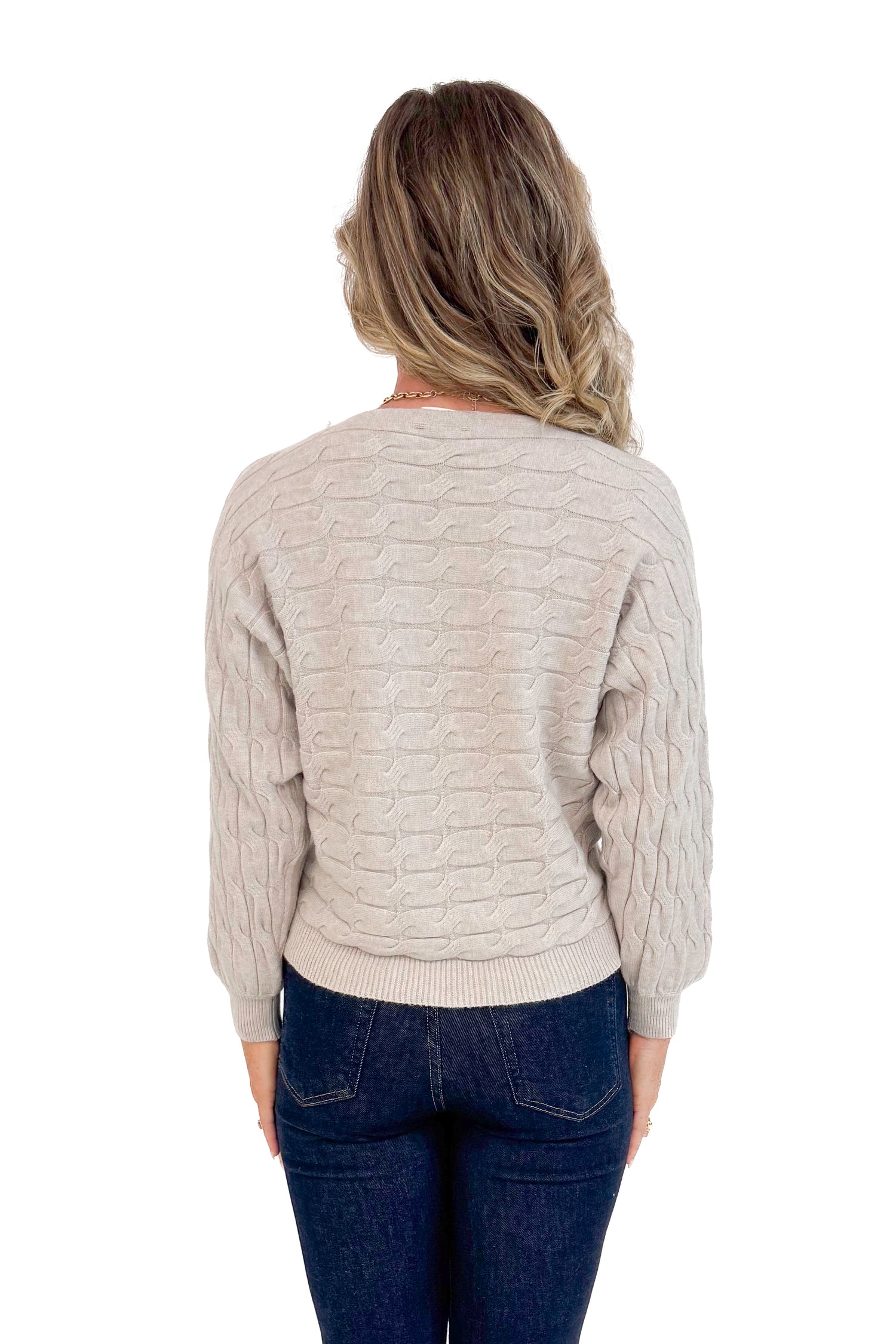 Studio back picture of woman wearing Oat Cable Knit Dolman Sweater and jeans with white background.