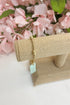Gold bracelet with a tag on a beige stand against a pink floral background