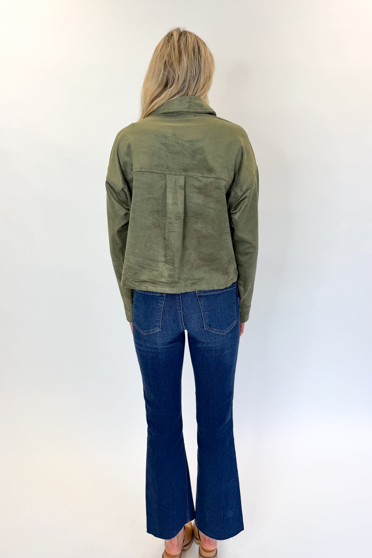 Back view of woman wearing Swagger Boutique’s Monstera All Day Cropped Suede Jacket by Z Supply with jeans against white studio background.