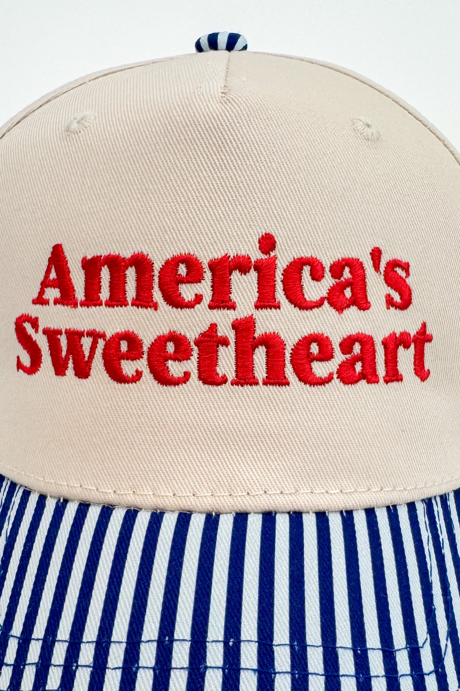 Close-up of the “America’s Sweetheart” embroidery on the front of the striped-brim cap.