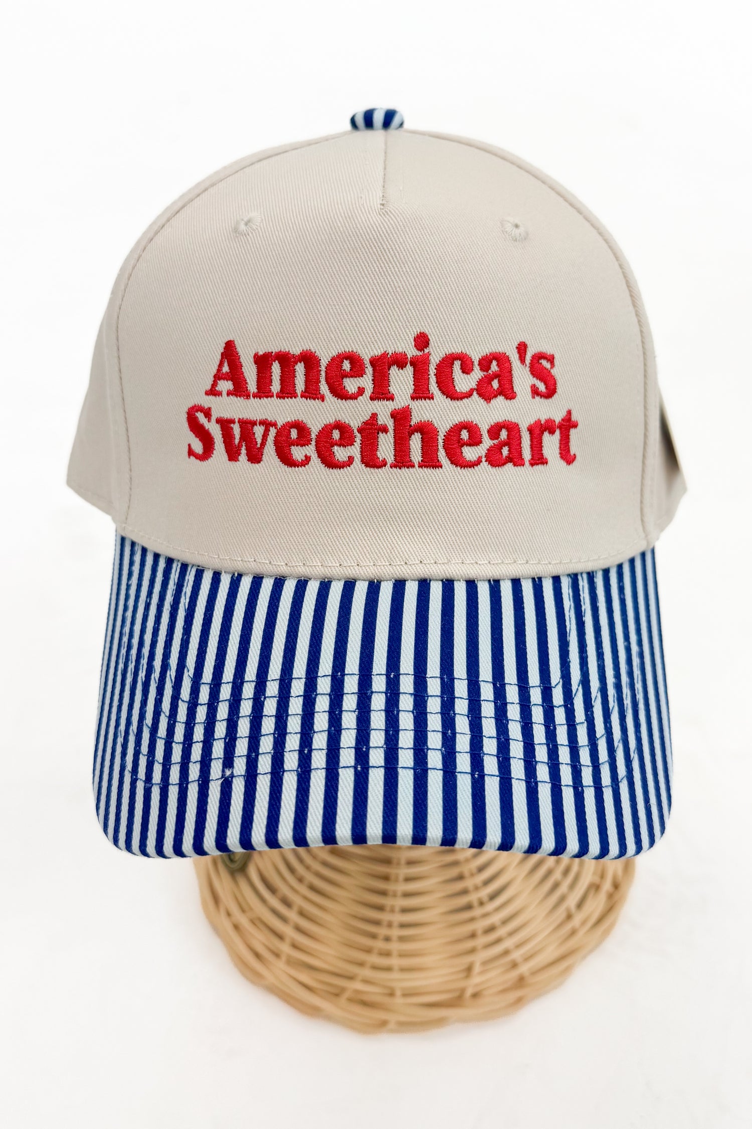 Front view of a striped-brim trucker hat with “America’s Sweetheart” embroidered on the front. 