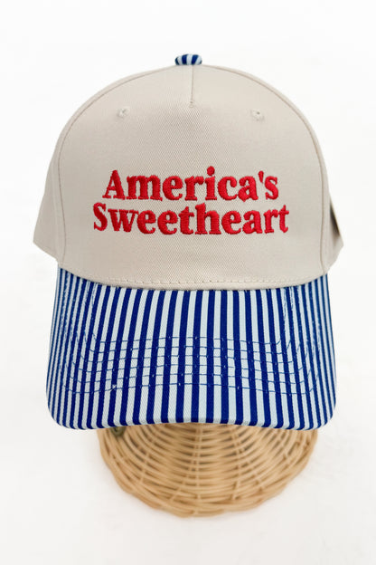 Front view of a striped-brim trucker hat with “America’s Sweetheart” embroidered on the front. 