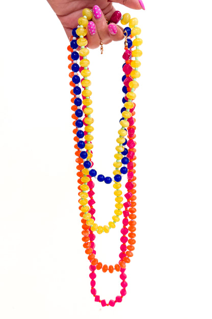 Colorful beaded necklaces held by a hand on a white background