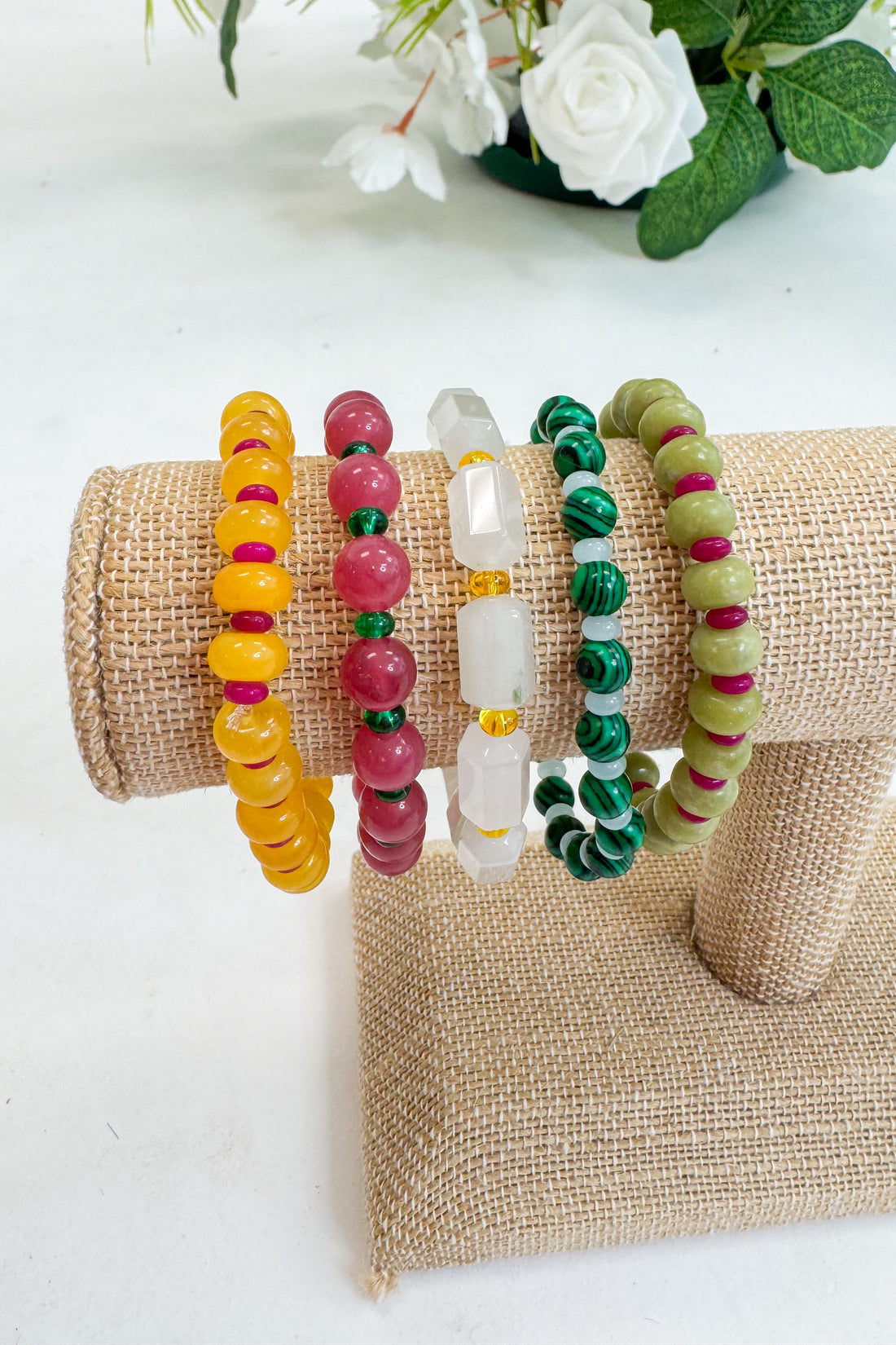 Set of colorful beaded bracelets on a textured surface with flowers in the background
