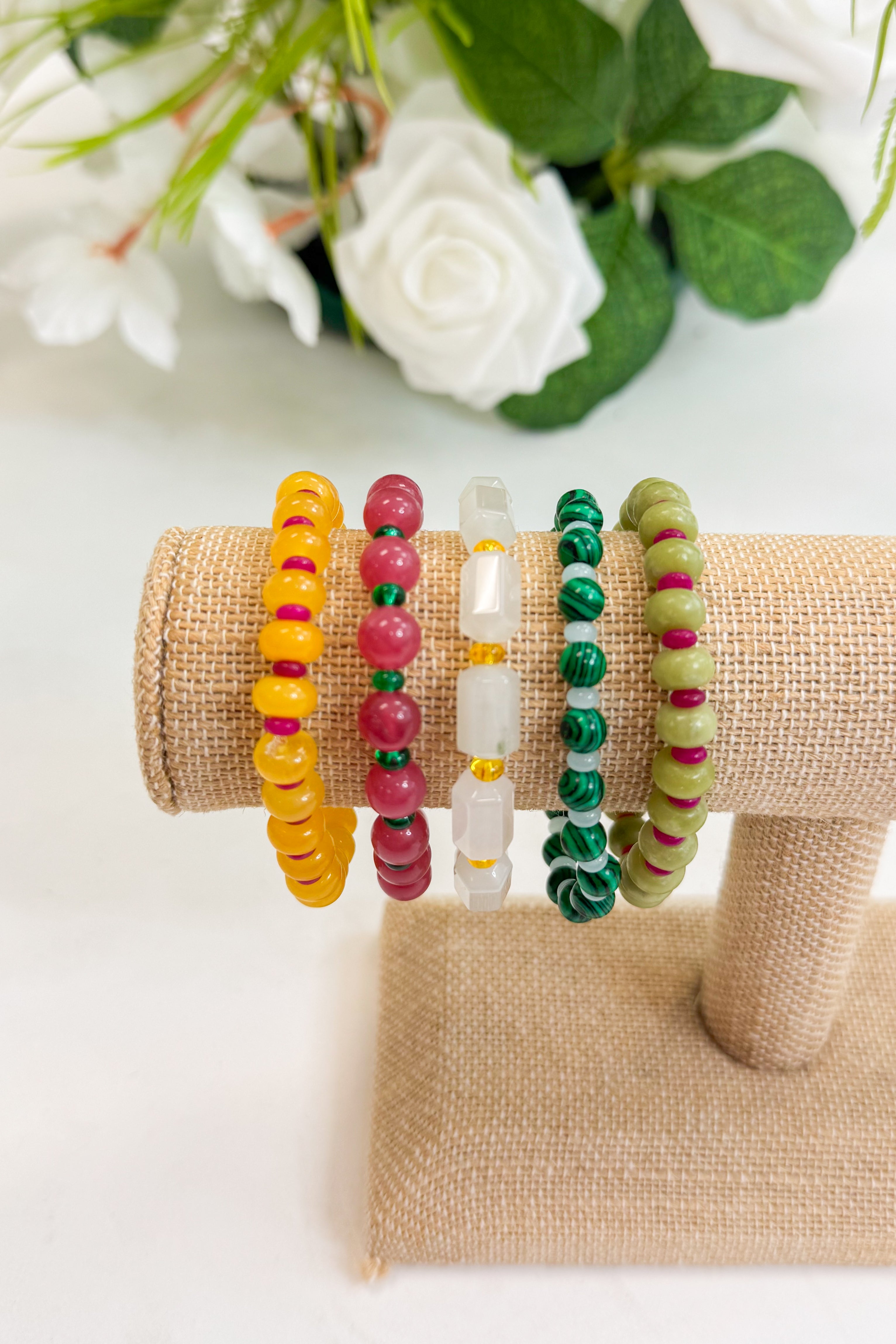 Set of colorful beaded bracelets on a burlap roll with flowers in the background