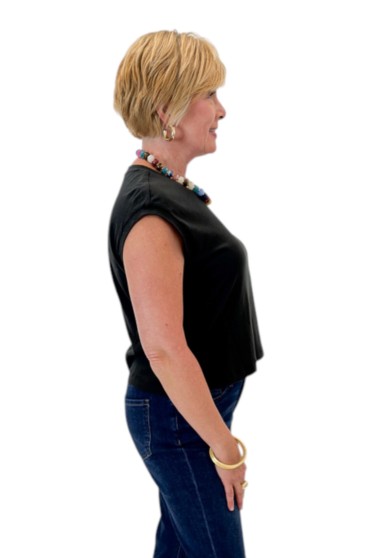 Side view of woman wearing Swagger Boutique’s Ash Black Flex Sleeveless Tee by Z Supply with jeans against white studio background.