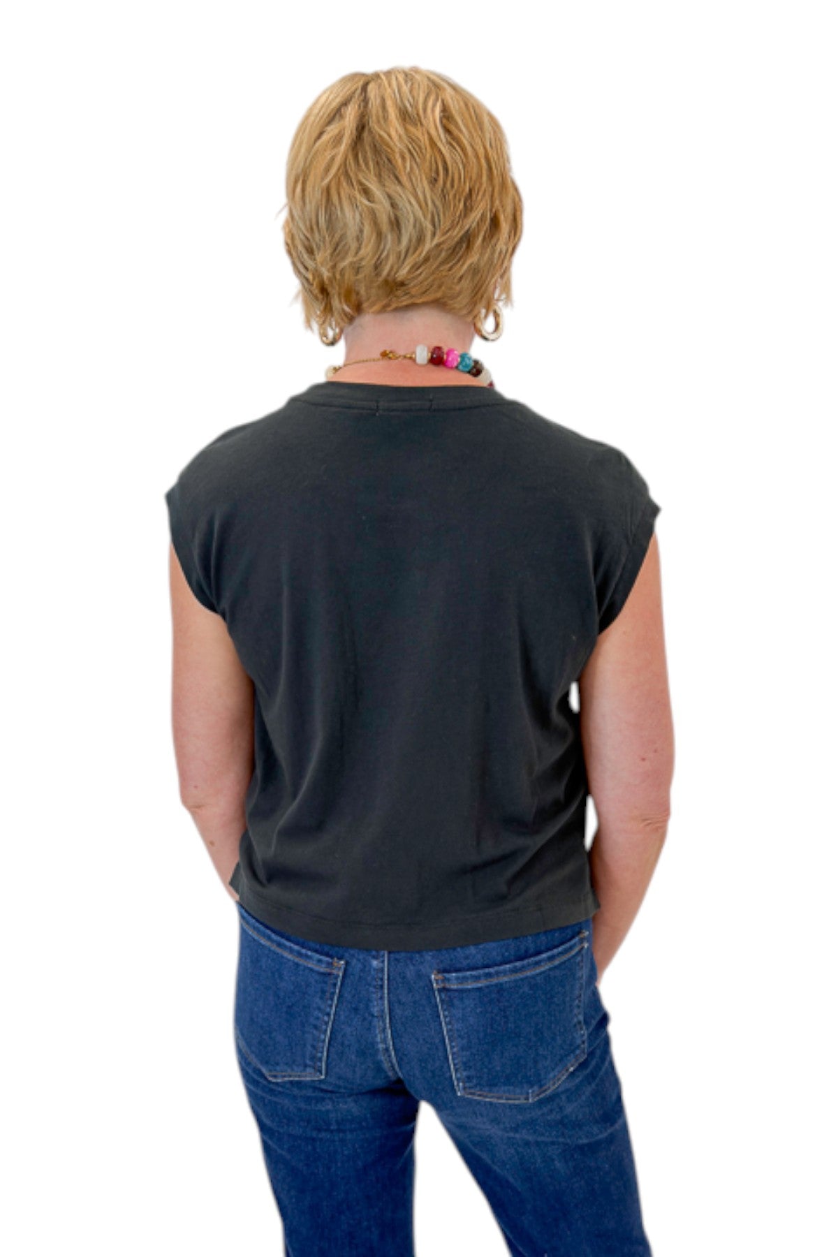 Back view of woman wearing Swagger Boutique’s Ash Black Flex Sleeveless Tee by Z Supply with jeans against white studio background.