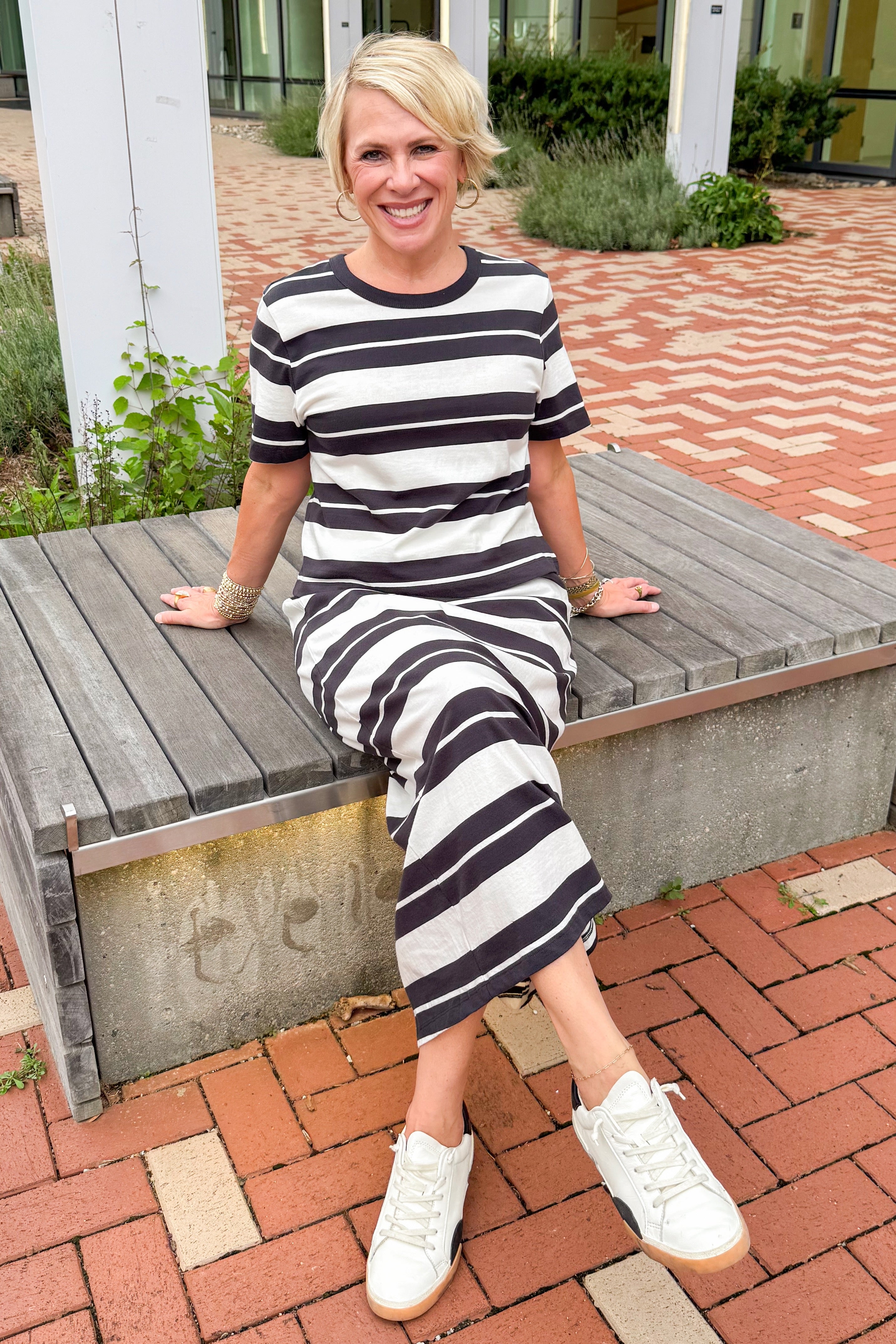 Front view of woman wearing Swagger Boutique’s Ash Black Stellan Striped Tee by Z Supply with Ash Black Gail Striped Jersey Midi Skirt by Z Supply sitting on a bench outside. 