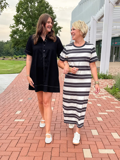 Front view of women wearing Swagger Boutique’s Ash Black Stellan Striped Tee by Z Supply with Ash Black Gail Striped Jersey Midi Skirt by Z Supply and black stitch detail dress walking down a red brick path. 