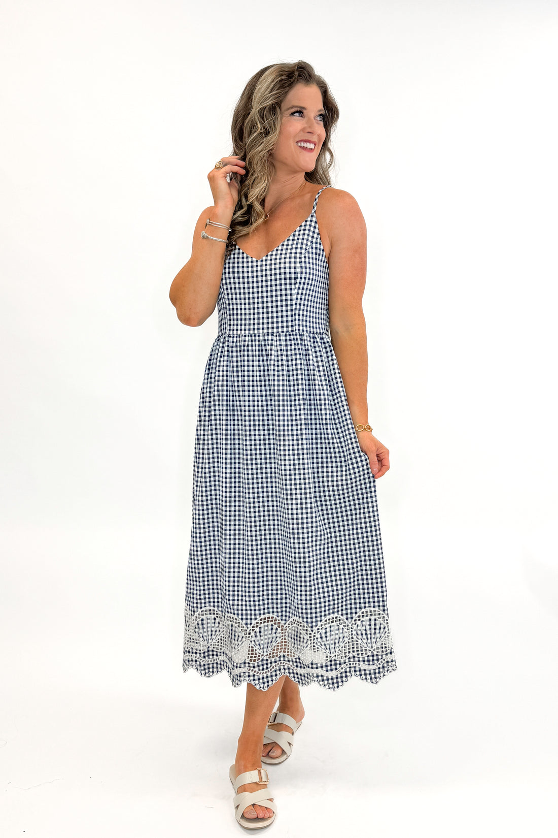 Front view of woman wearing Navy Gingham With Shell Embroidery Dress with sandals against white studio background.