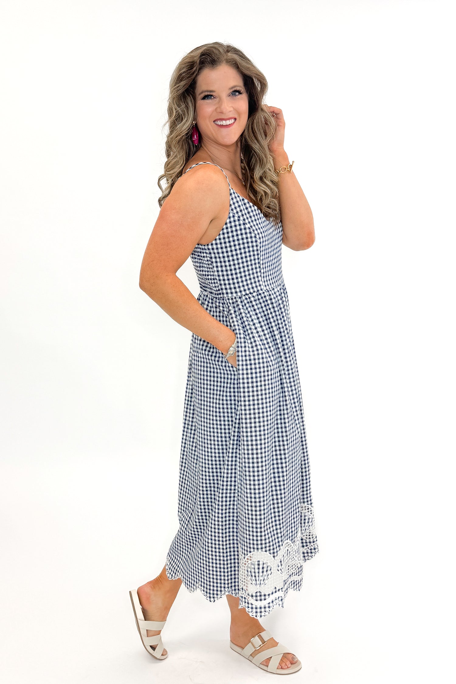 Side view of woman wearing Navy Gingham With Shell Embroidery Dress with sandals against white studio background.