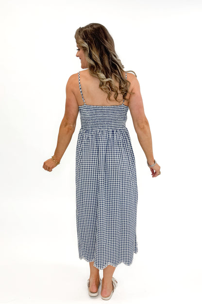 Back view of woman wearing Navy Gingham With Shell Embroidery Dress with sandals against white studio background.
