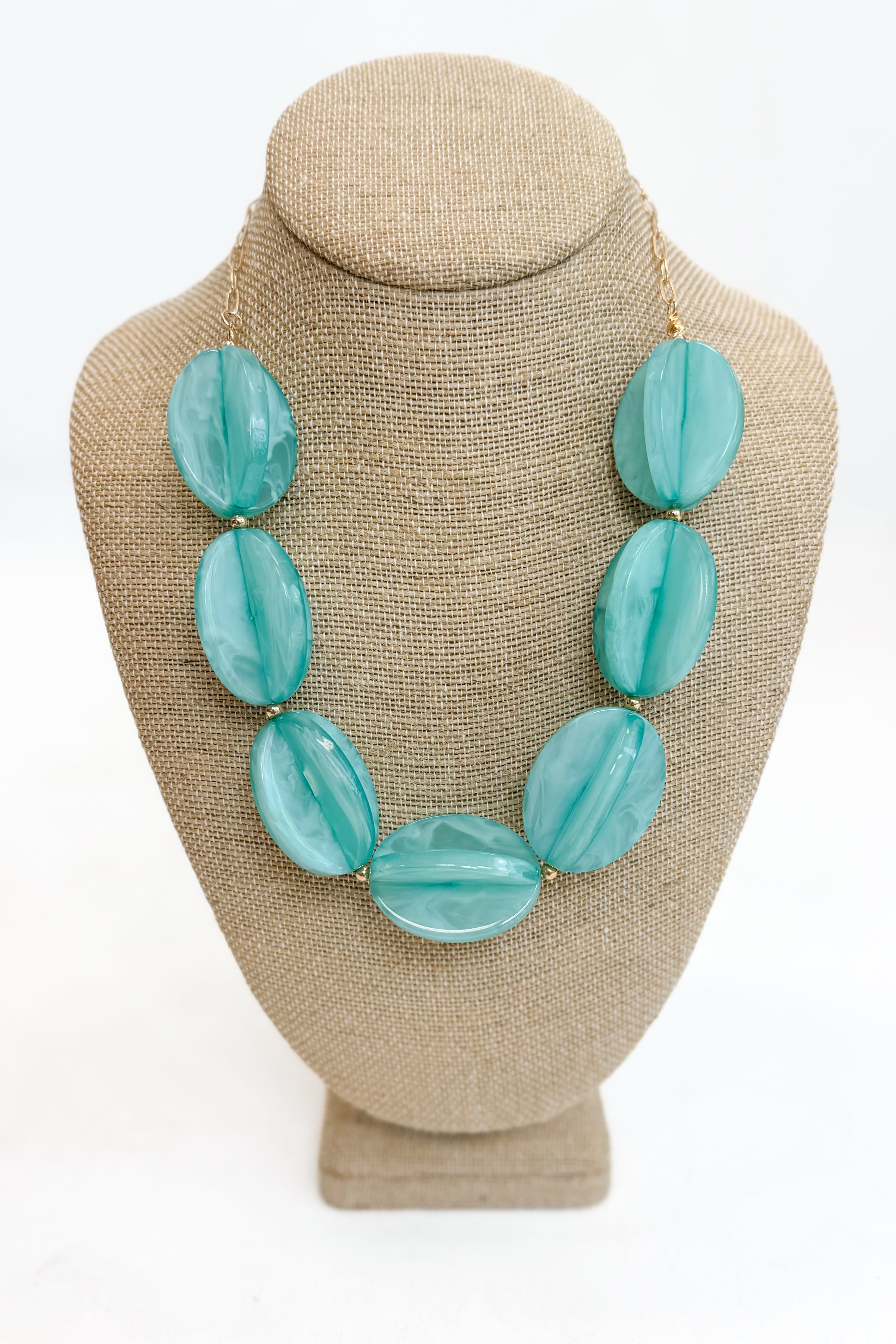 Turquoise necklace on a beige bust against a white background