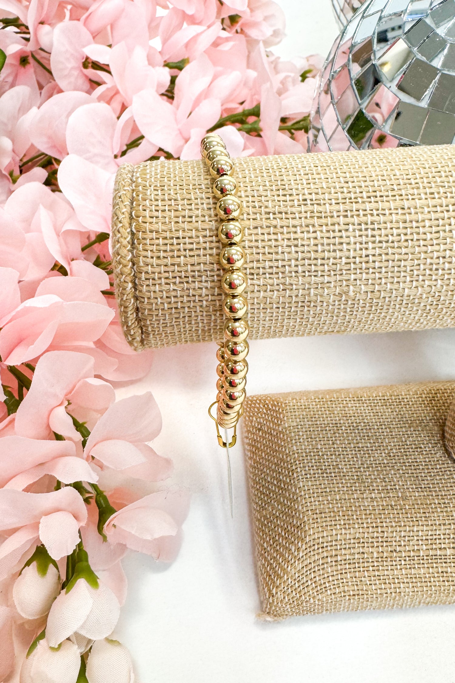 Gold beaded bracelet on a beige fabric with pink flowers in the background