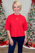 Woman in a red sweater and blue pants standing in front of Christmas trees with decorations.