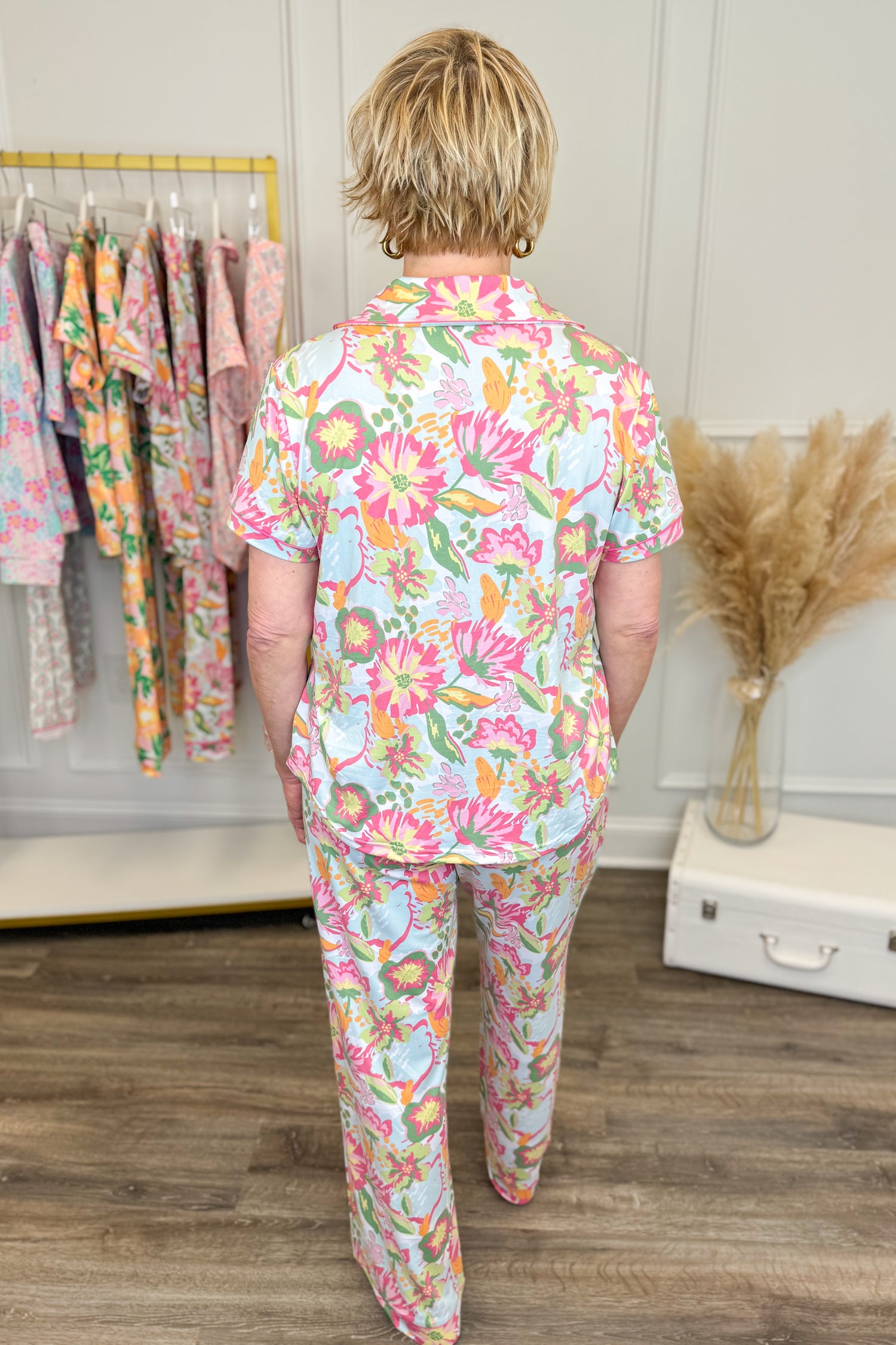 Person wearing a colorful floral pajama set standing in a room with a rack of clothes and decorative elements.