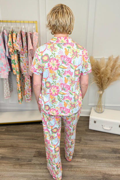 Person wearing a colorful floral pajama set standing in a room with a rack of clothes and decorative elements.