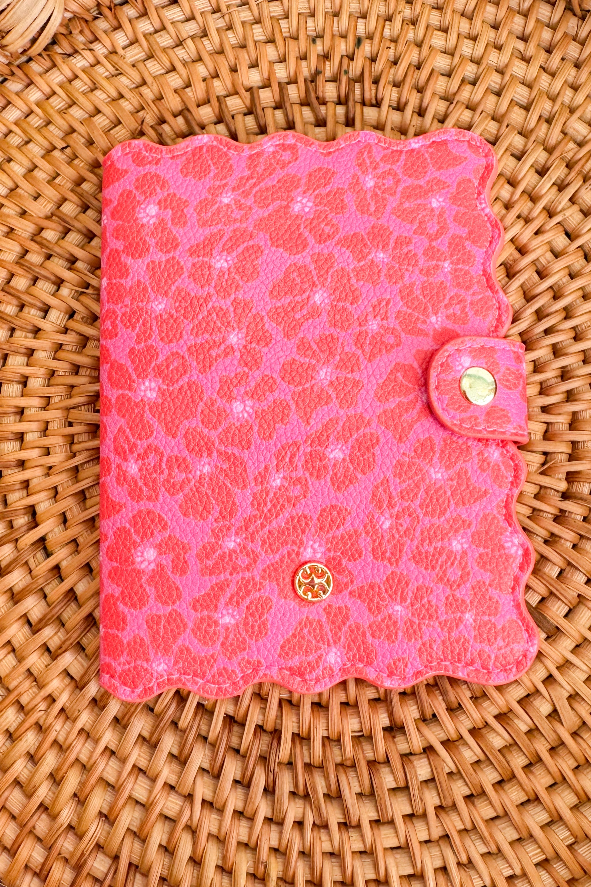 Pink textured notebook with a gold logo on a wicker surface