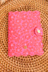 Pink textured notebook with a gold logo on a wicker surface
