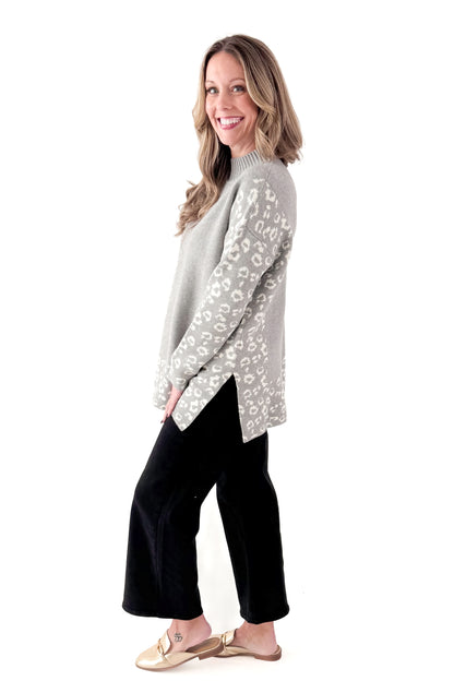 Side view of woman wearing Grey Leopard Print Lined Sweater with jeans against white studio background.
