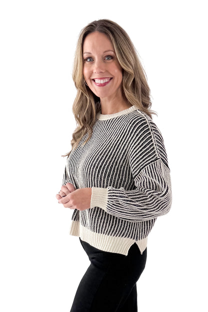 Side view of woman wearing Black &amp; Cream Striped Sweater with jeans against white studio background.