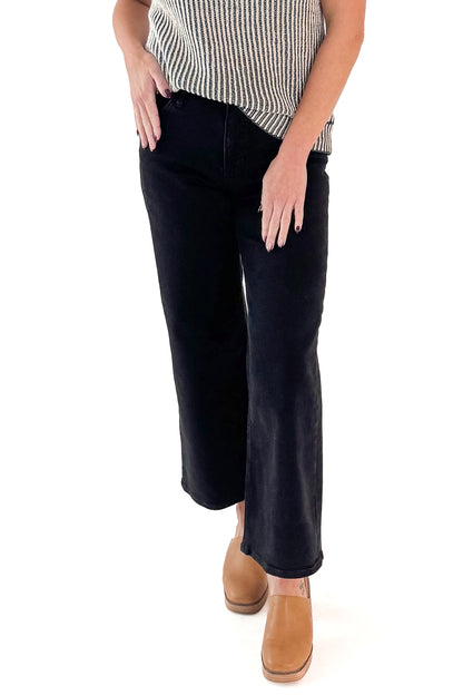 Front view of woman wearing top with black wide leg jeans against white studio background.