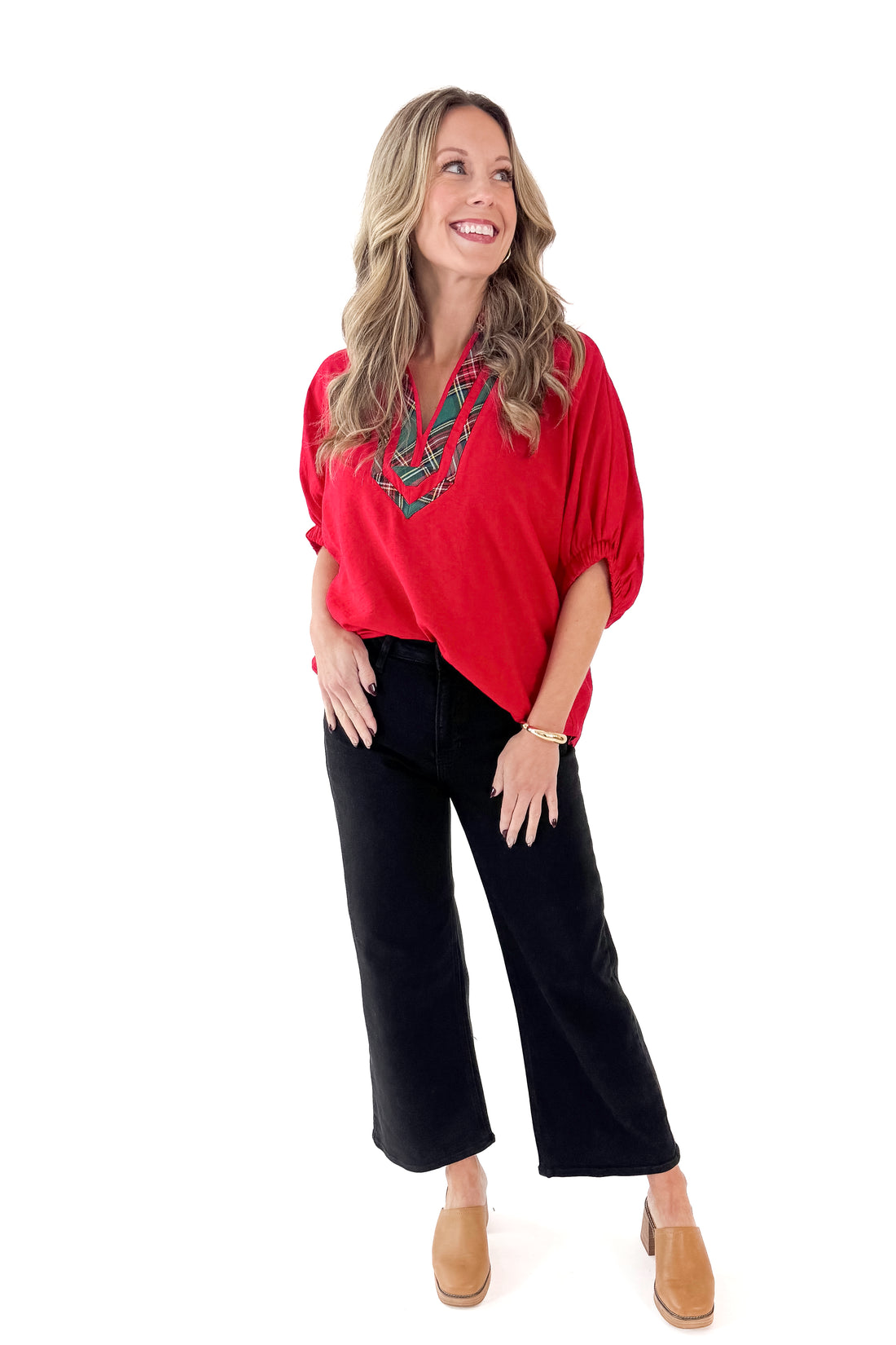 Front view of woman wearing red top with black wide leg jeans against white studio background.