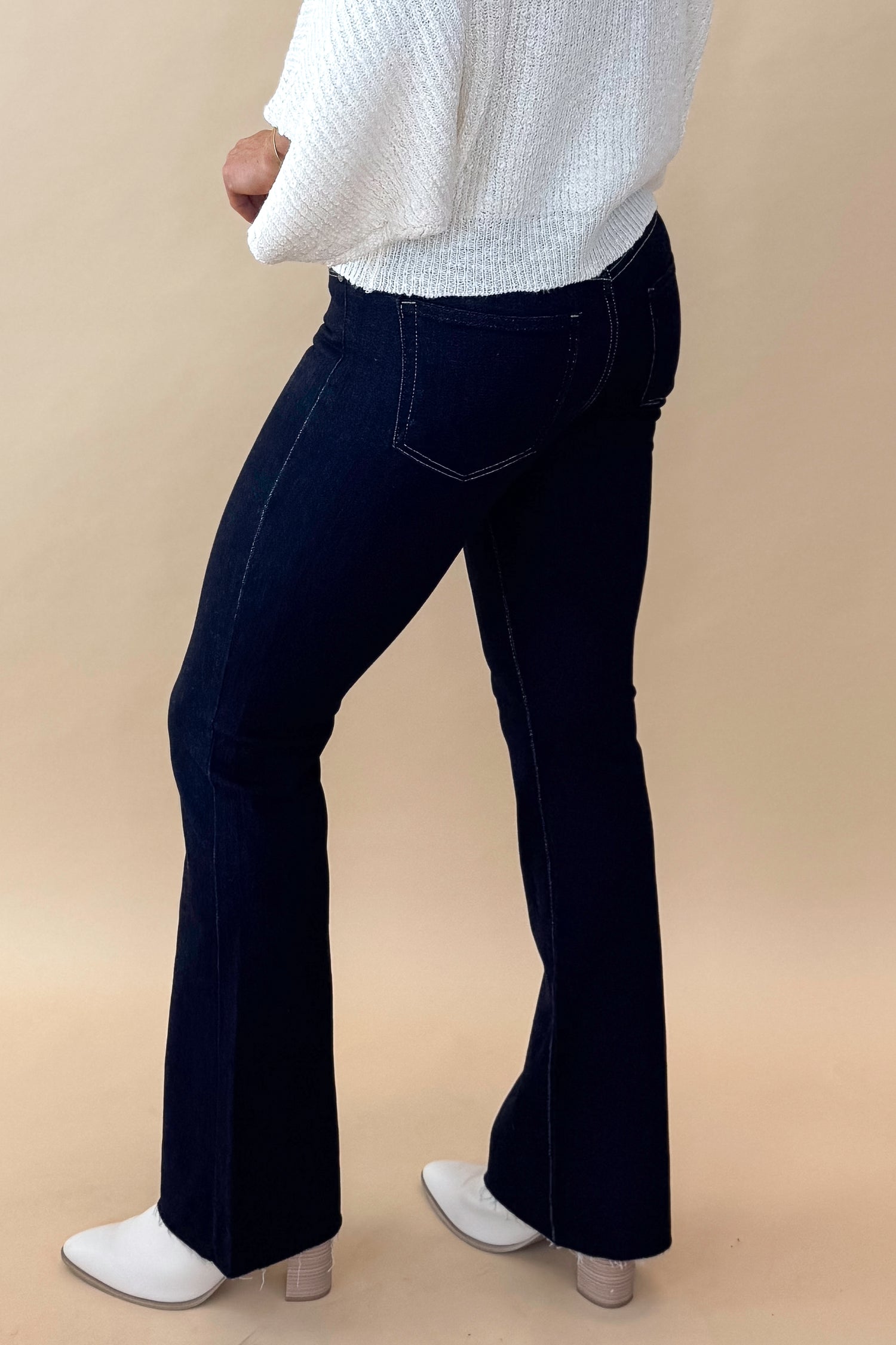 Side view of model wearing top with Super Dark Wash Flare Jeans  against tan studio background.