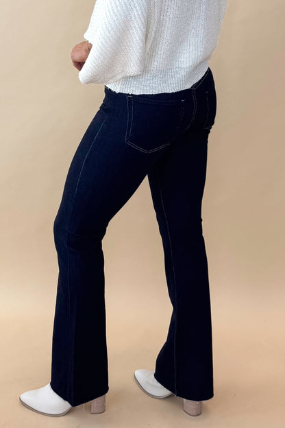 Side view of model wearing top with Super Dark Wash Flare Jeans  against tan studio background.