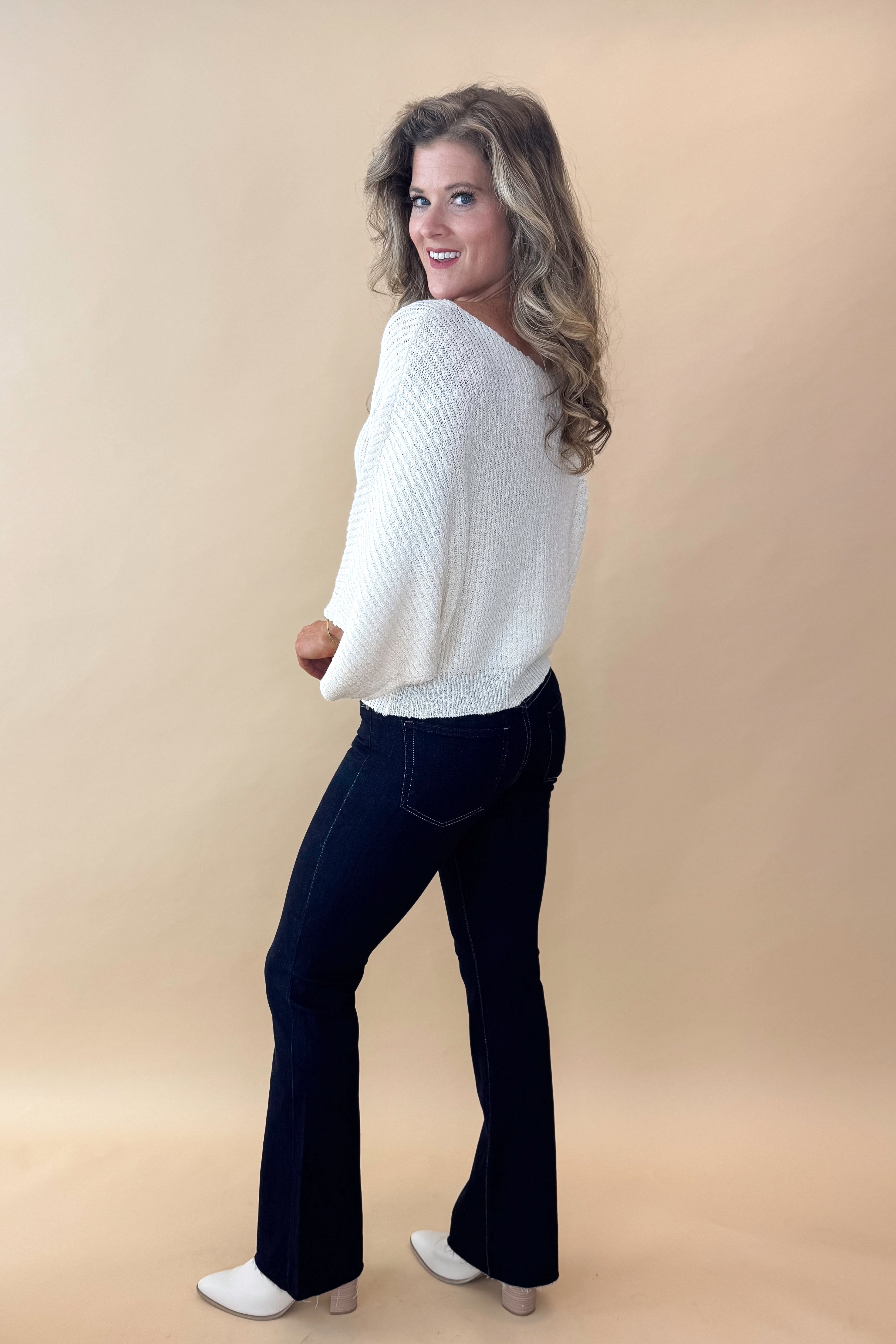 Side view of model wearing top with Super Dark Wash Flare Jeans  against tan studio background.