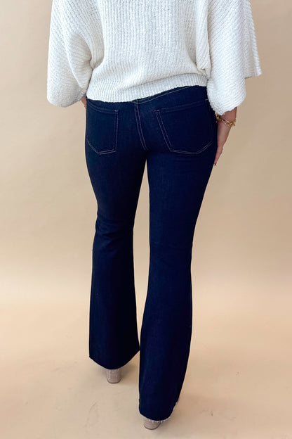 Back view of model wearing top with Super Dark Wash Flare Jeans  against tan studio background.
