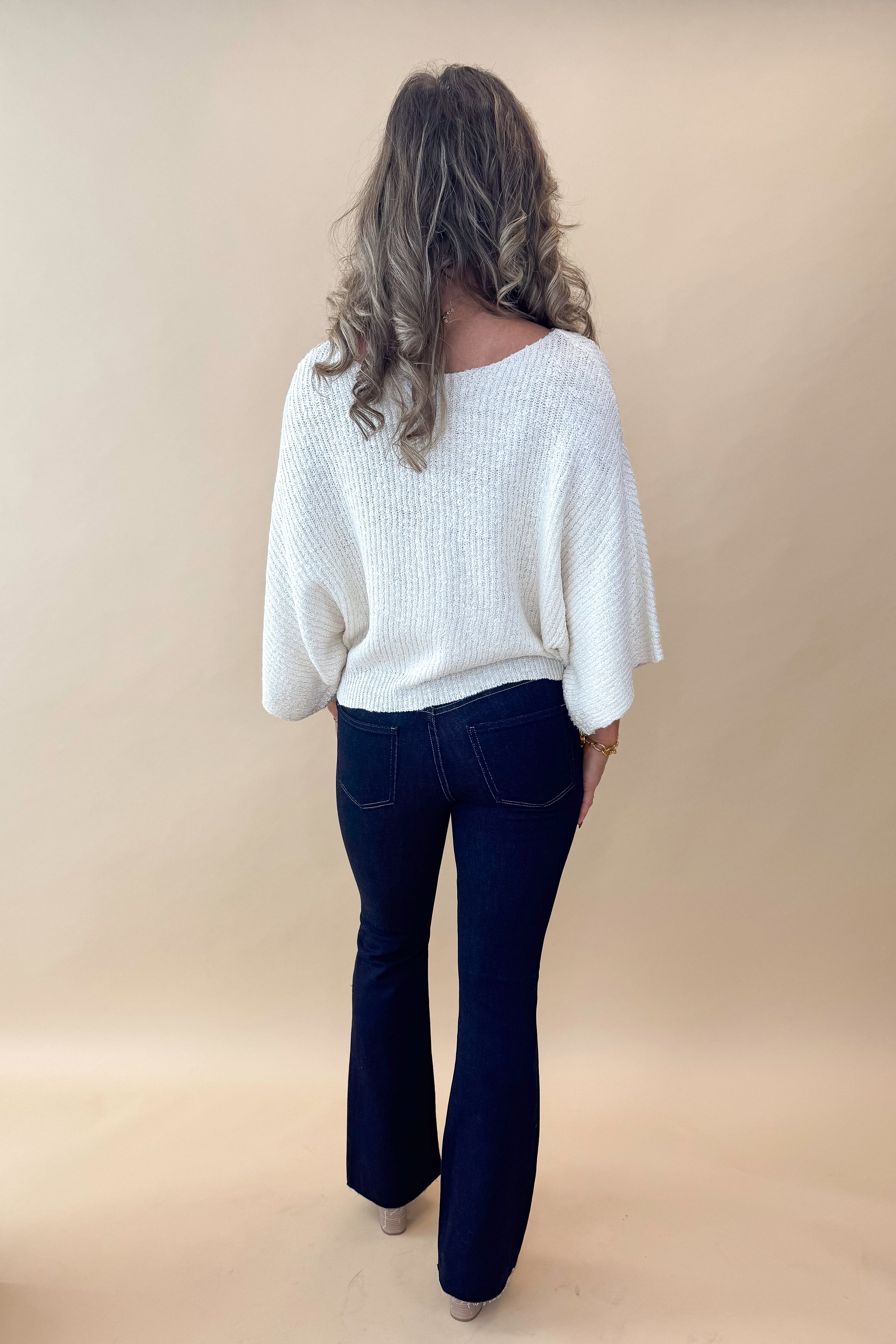 Back view of model wearing top with Super Dark Wash Flare Jeans  against tan studio background.