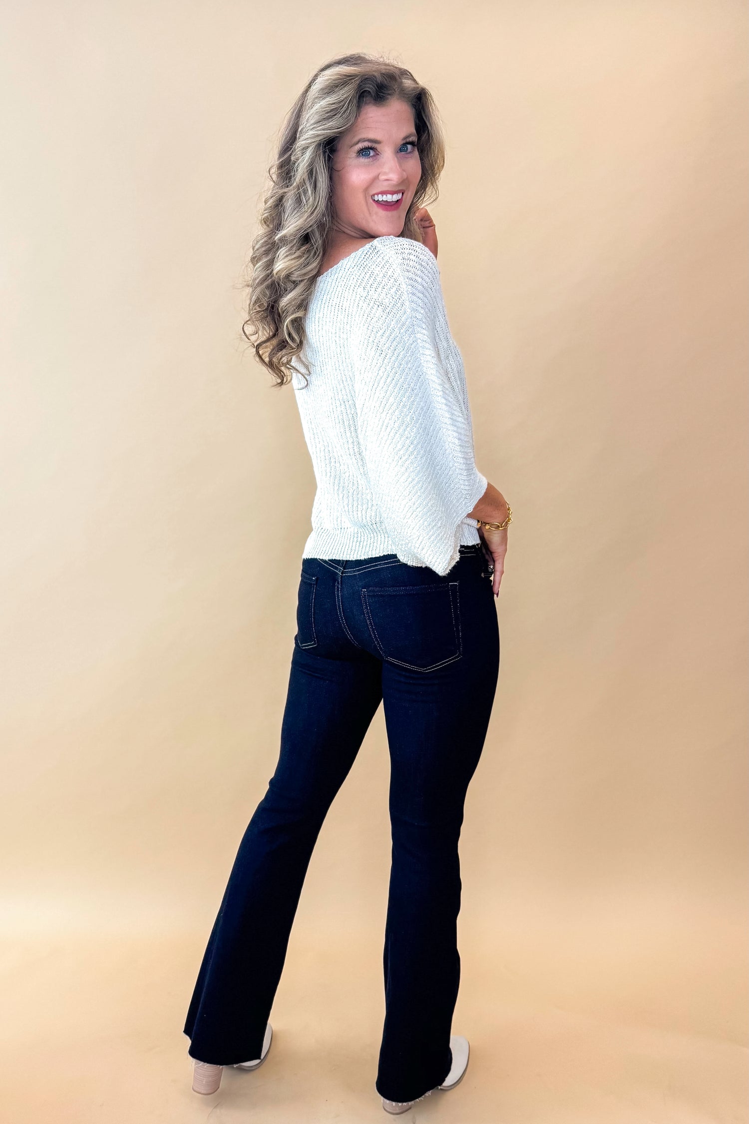 Side view of model wearing top with Super Dark Wash Flare Jeans  against tan studio background.