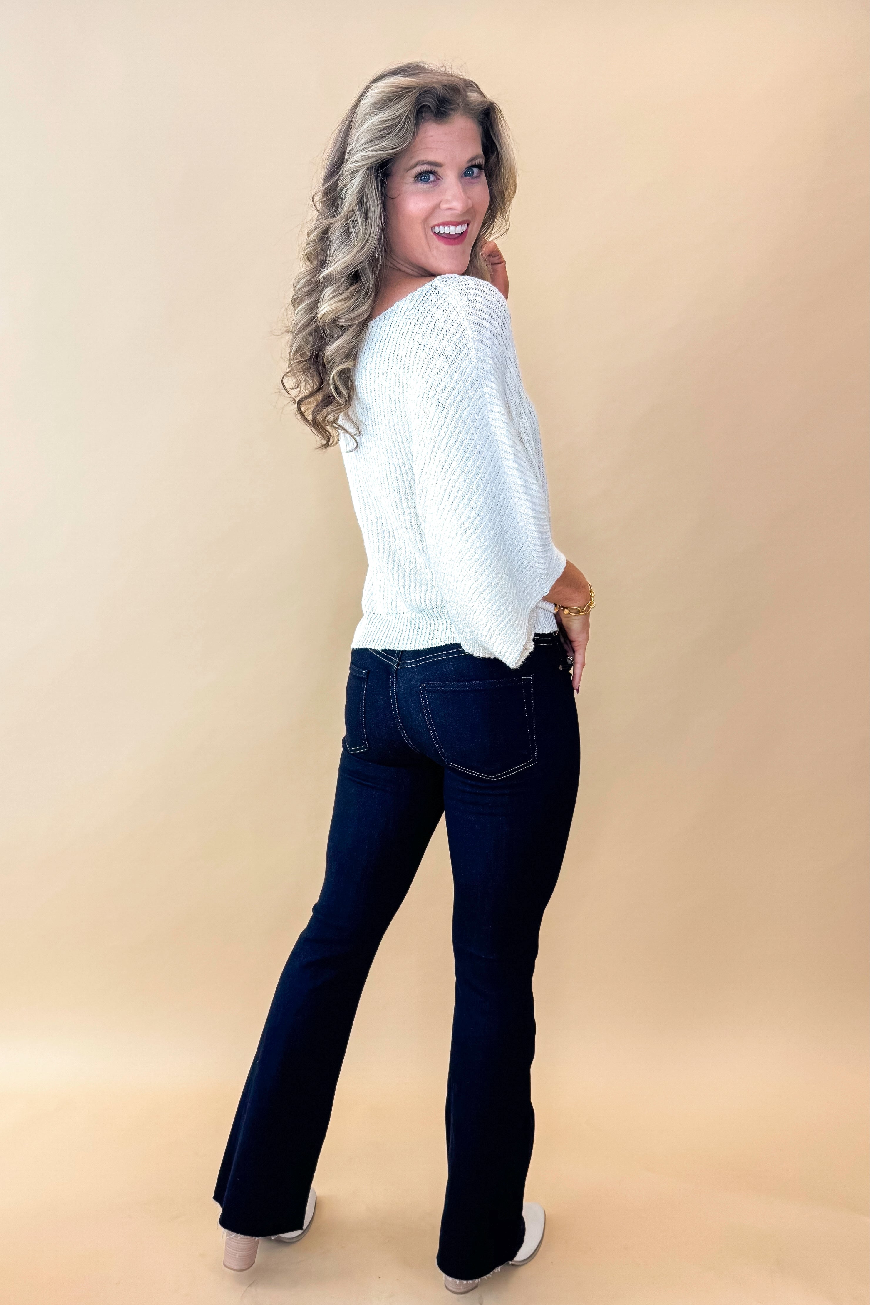 Side view of model wearing top with Super Dark Wash Flare Jeans  against tan studio background.