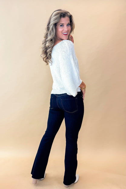 Side view of model wearing top with Super Dark Wash Flare Jeans  against tan studio background.