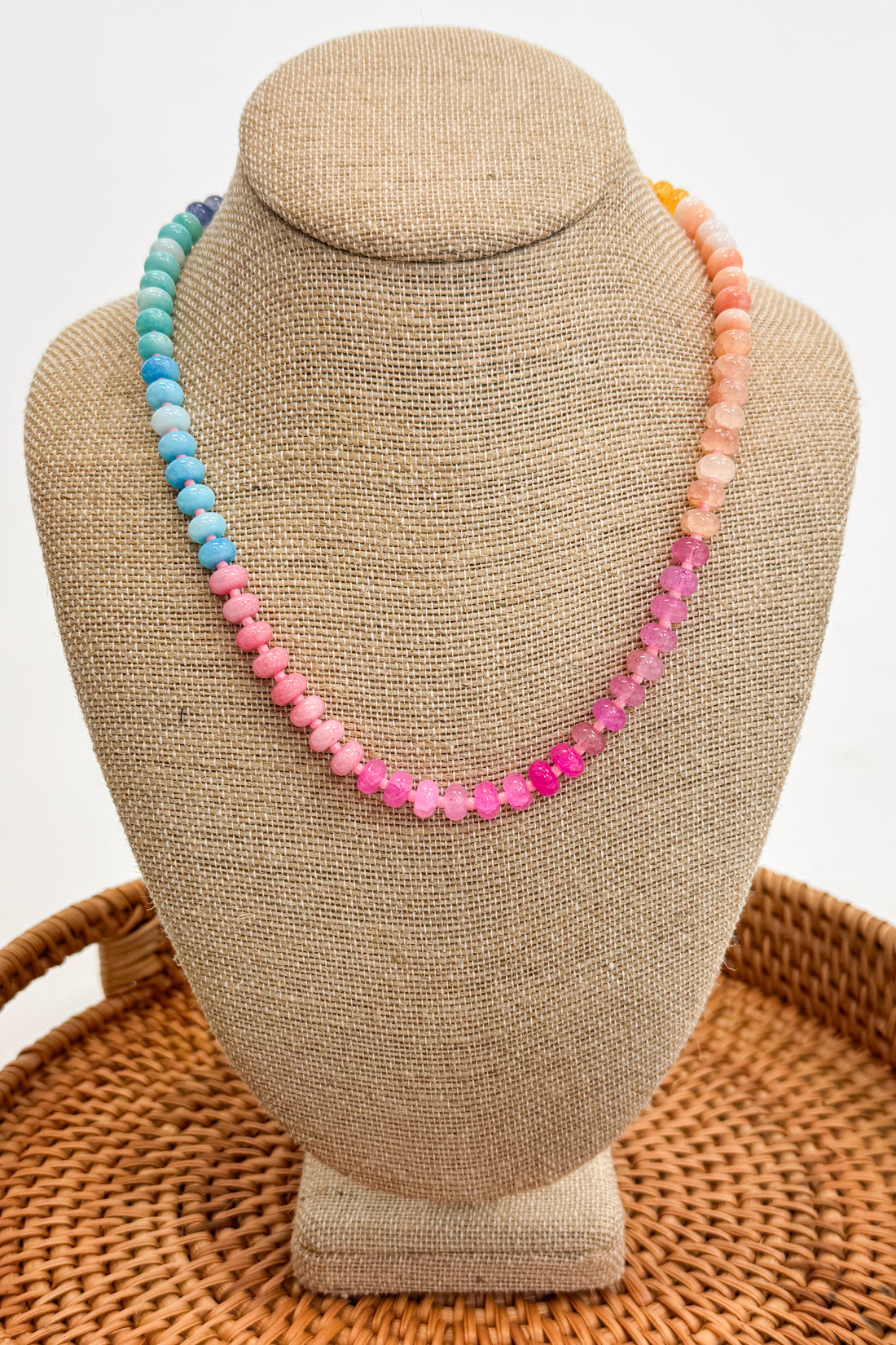 Colorful beaded necklace on a beige jewelry display stand with a woven surface below.