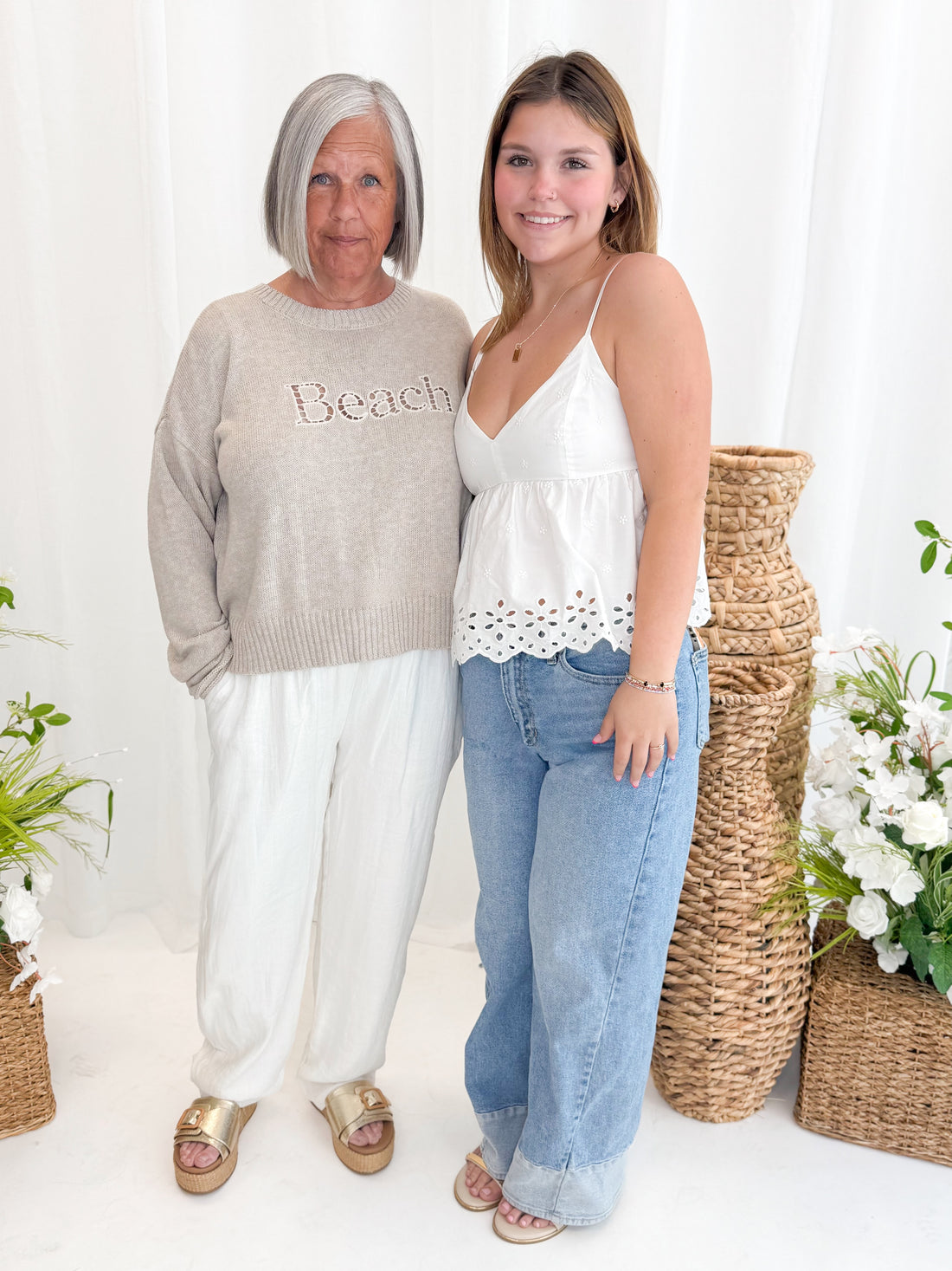 Front view of woman wearing Swagger Boutique’s Natural Heather Beach Embroidered Sweater by Z Supply with white pants and daughter wearing white eyelet tank against white decorative background.