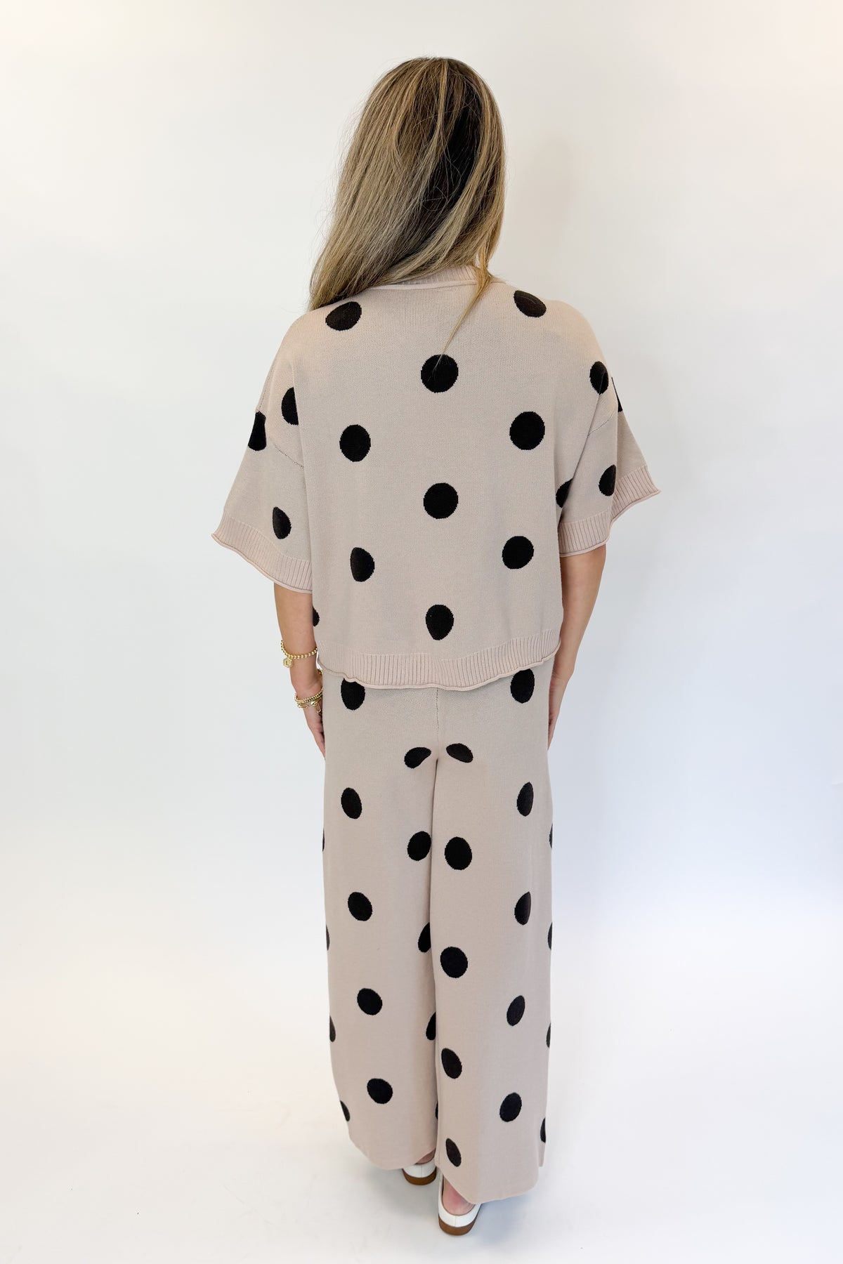 Back view of woman wearing Swagger Boutique’s Beige Polka Dot Short Sleeve Top &amp; Knit Pants against white studio background.