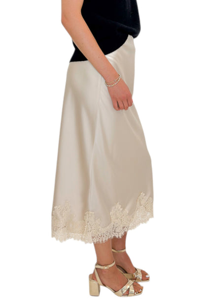 Side detail view of woman wearing Swagger Boutique’s Beige Satin &amp; Lace Midi Skirt with heels against white studio background.