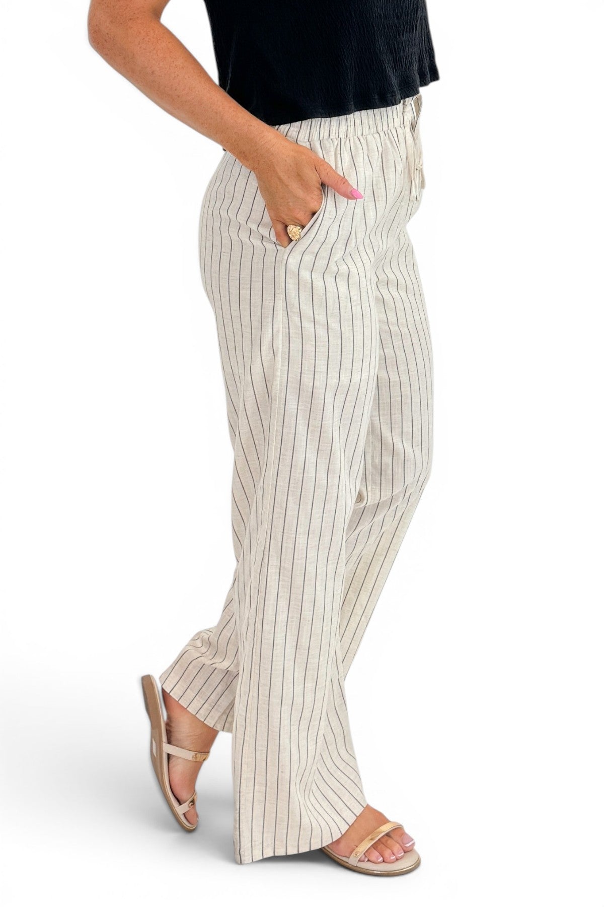 Side detail view of woman wearing Swagger Boutique’s Beige Striped Wide Leg Linen Pants with top against white studio background.