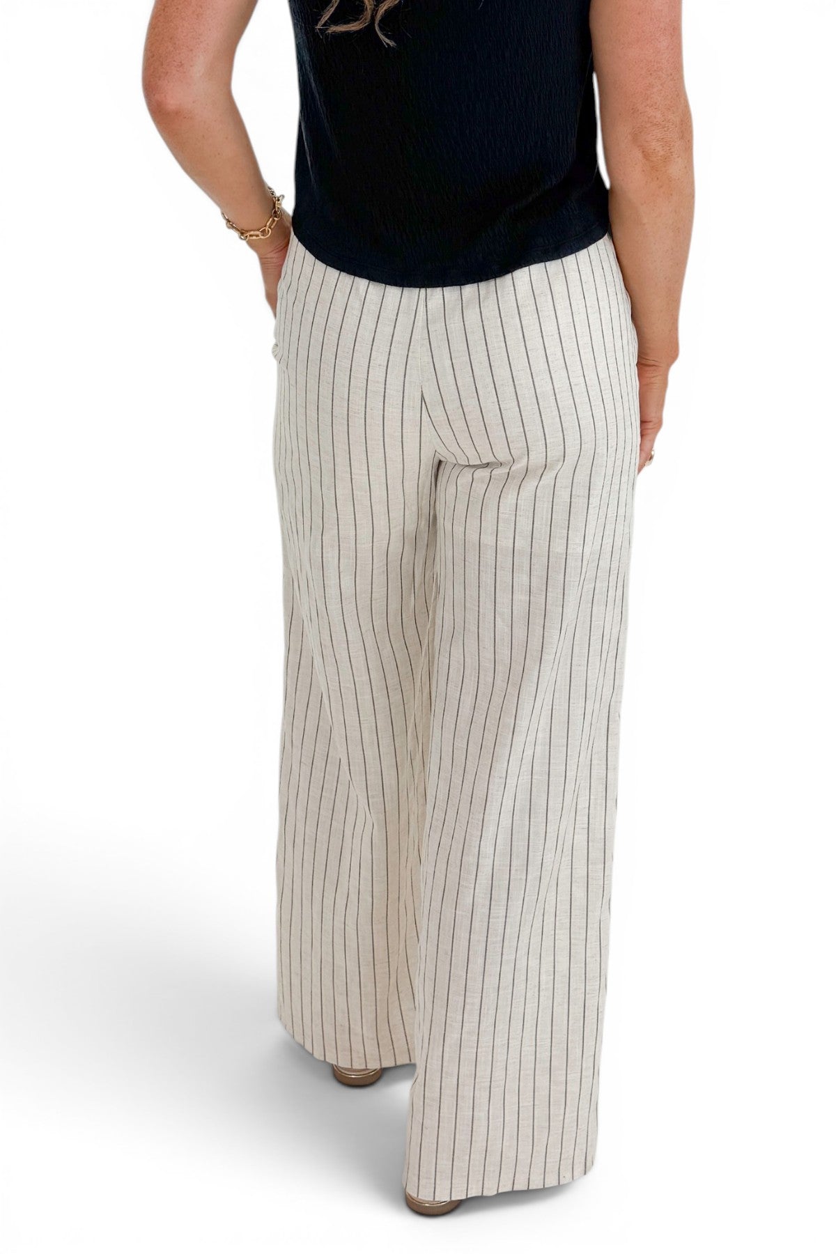 Back view of woman wearing Swagger Boutique’s Beige Striped Wide Leg Linen Pants with top against white studio background.