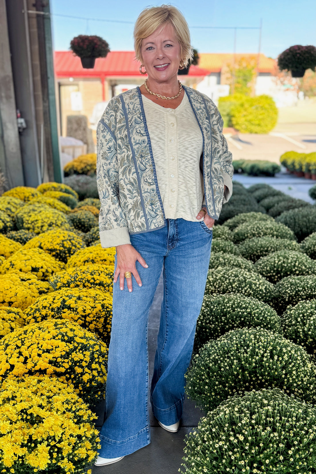 Front view of woman wearing Swagger Boutique’s Beige &amp; Blue Printed Lightweight Jacket, Cream Sleeveless Button up Sweater with Maya Denim Jeans at a garden center.