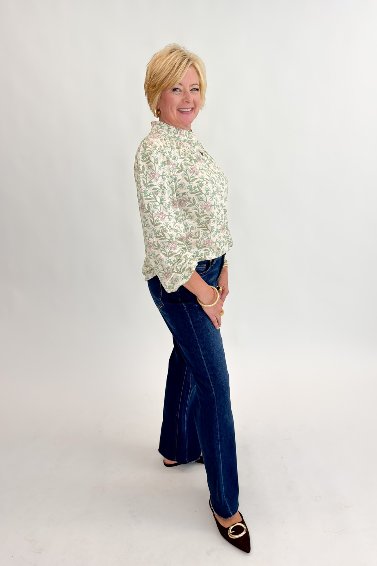 Side view of woman wearing Swagger Boutique’s Beige &amp; Olive Floral Long Sleeve Top with jeans against white studio background.