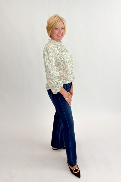 Side view of woman wearing Swagger Boutique’s Beige &amp; Olive Floral Long Sleeve Top with jeans against white studio background.