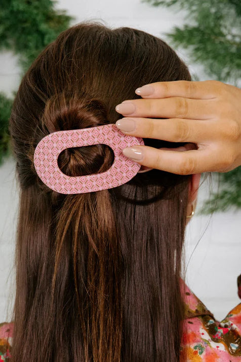 Person holding a pink hair clip in front of their hair with a blurred background