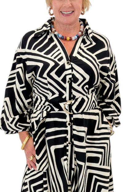Front detail view of woman wearing Swagger Boutique’s Black Abstract Print Midi Dress by Entro with heels against white studio background.