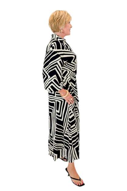 Side view of woman wearing Swagger Boutique’s Black Abstract Print Midi Dress by Entro with heels against white studio background.