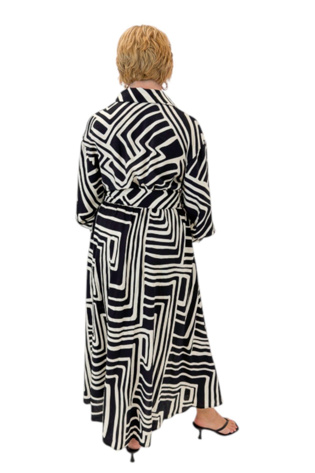 Back view of woman wearing Swagger Boutique’s Black Abstract Print Midi Dress by Entro with heels against white studio background.