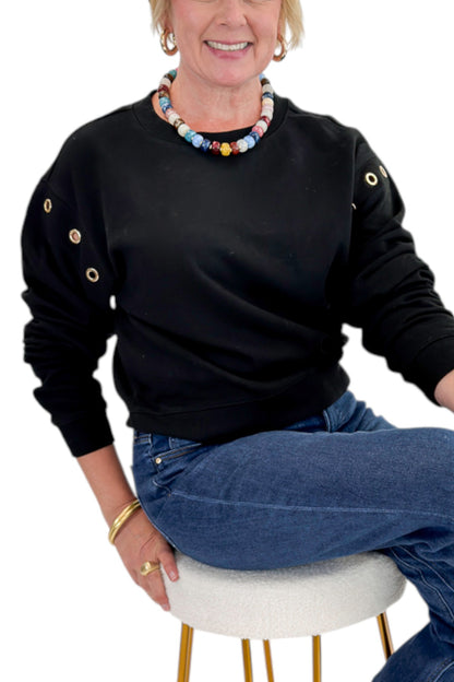 Front detail view of woman wearing Swagger Boutique’s Black Axel Grommet Sweatshirt by Z Supply with jeans against white studio background.